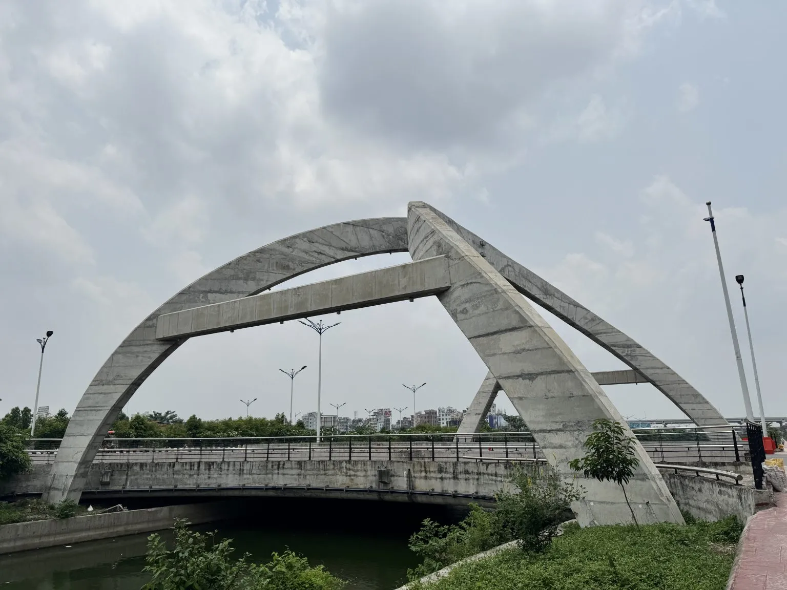 A concrete arch bridge beneath a cloudy sky, with a staircase and green vegetation below.