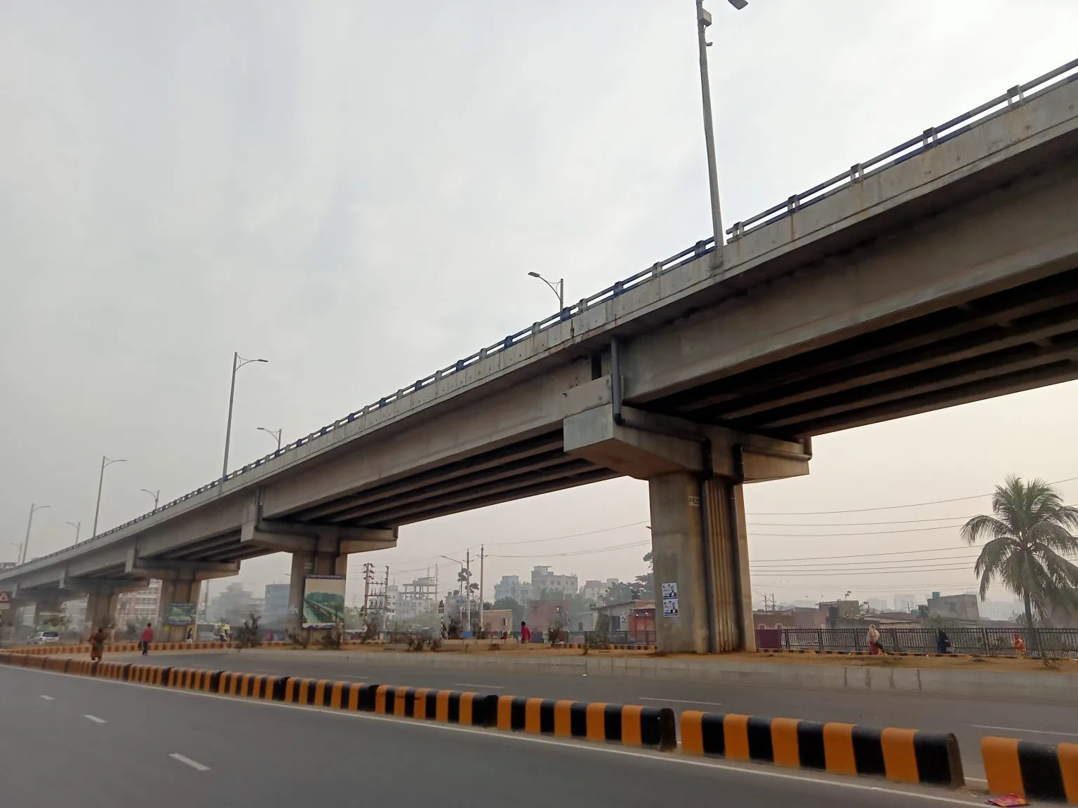 An elevated road curves above a street with black and yellow median barriers.