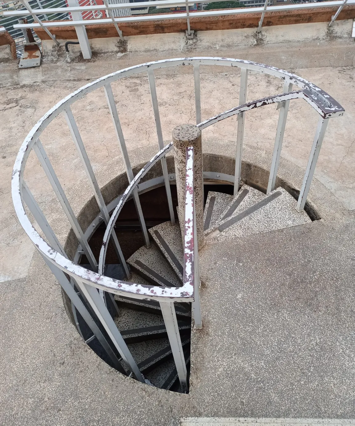 A spiral staircase with speckled treads and a weathered white handrail, viewed from above.